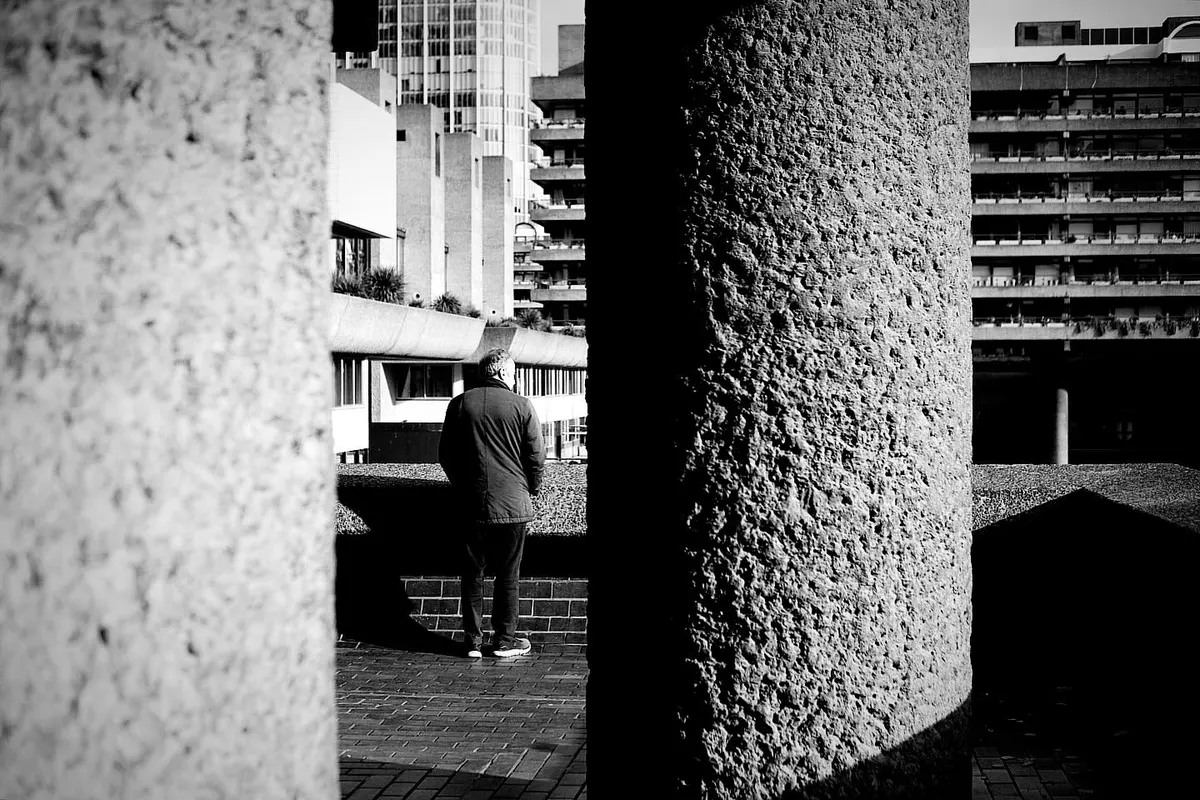 A figure framed between raw concrete columns at the Barbican, London